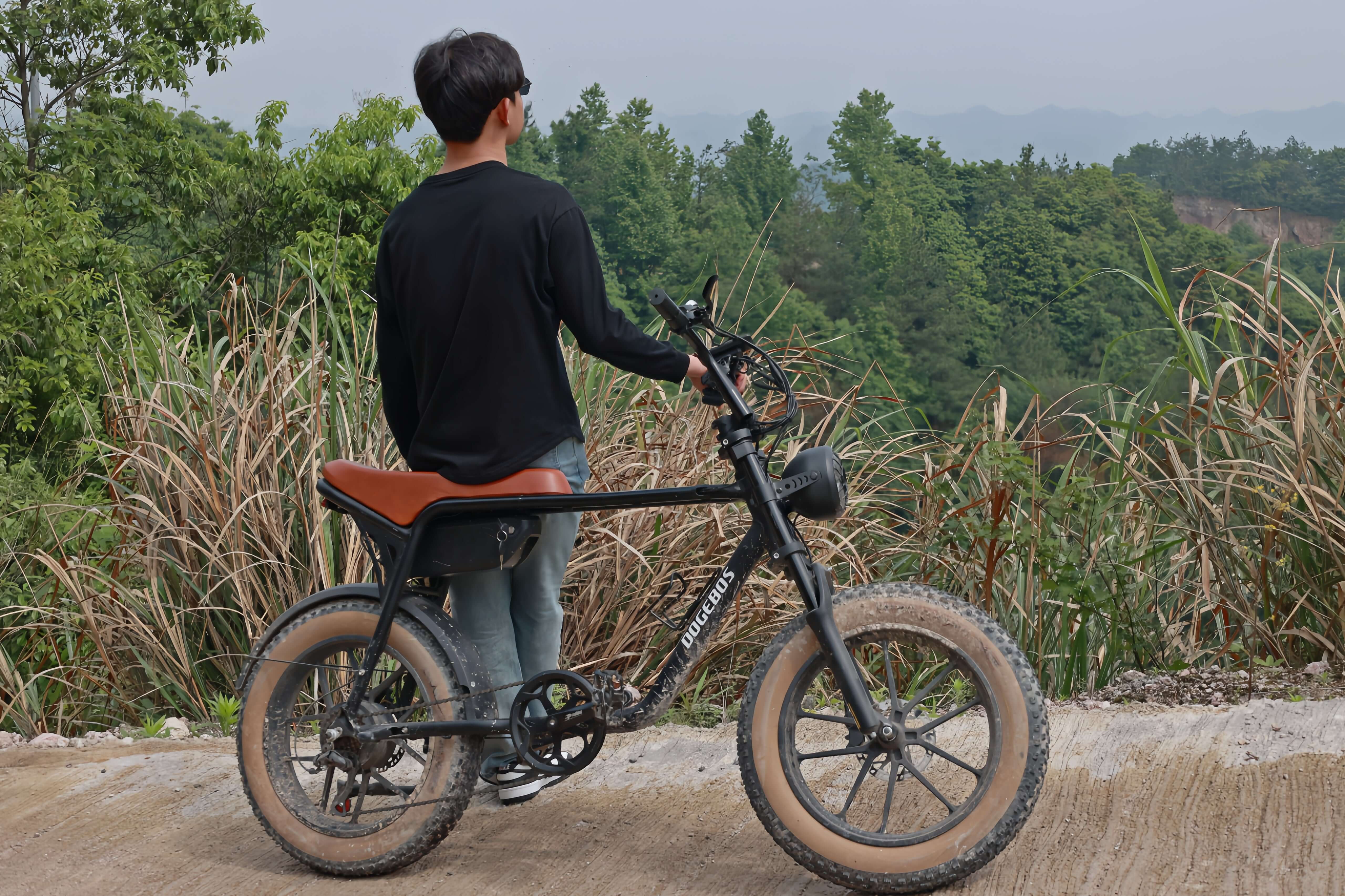 Model sitting on K3 electric bike, looking at mountain landscape